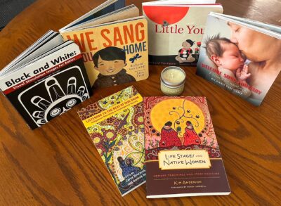 A bundle of six Indigenous books and children's books, plus a candle in a glass holder.
